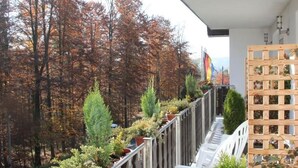 Un balcón con vistas a árboles otoñales, un enrejado de madera y una bandera.