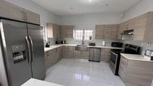 A modern kitchen with stainless steel appliances, light wood cabinets, and a white marble countertop. - Gulfview Townhouse With Pool and Jacuzzi (Diego Martin)
