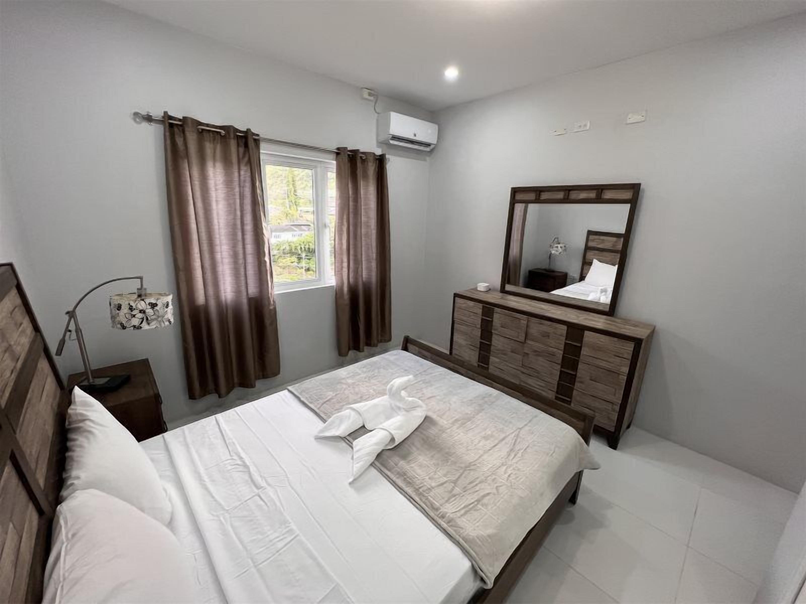 A bedroom with a bed, a dresser, a mirror, and a window with curtains.