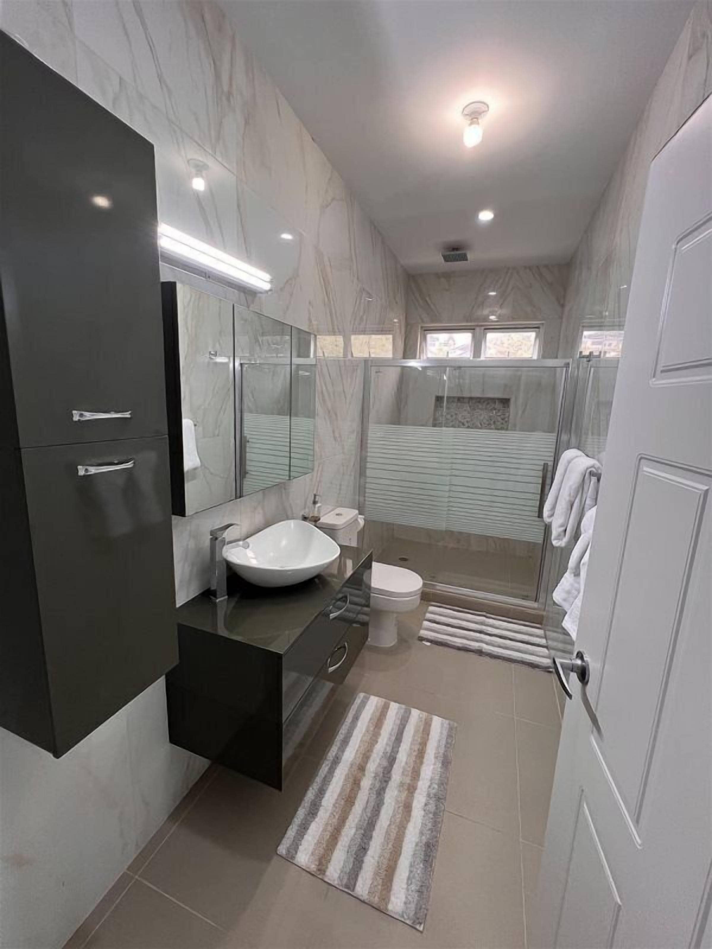 Un baño moderno con un espejo grande, un lavabo blanco, un inodoro y una zona de ducha.