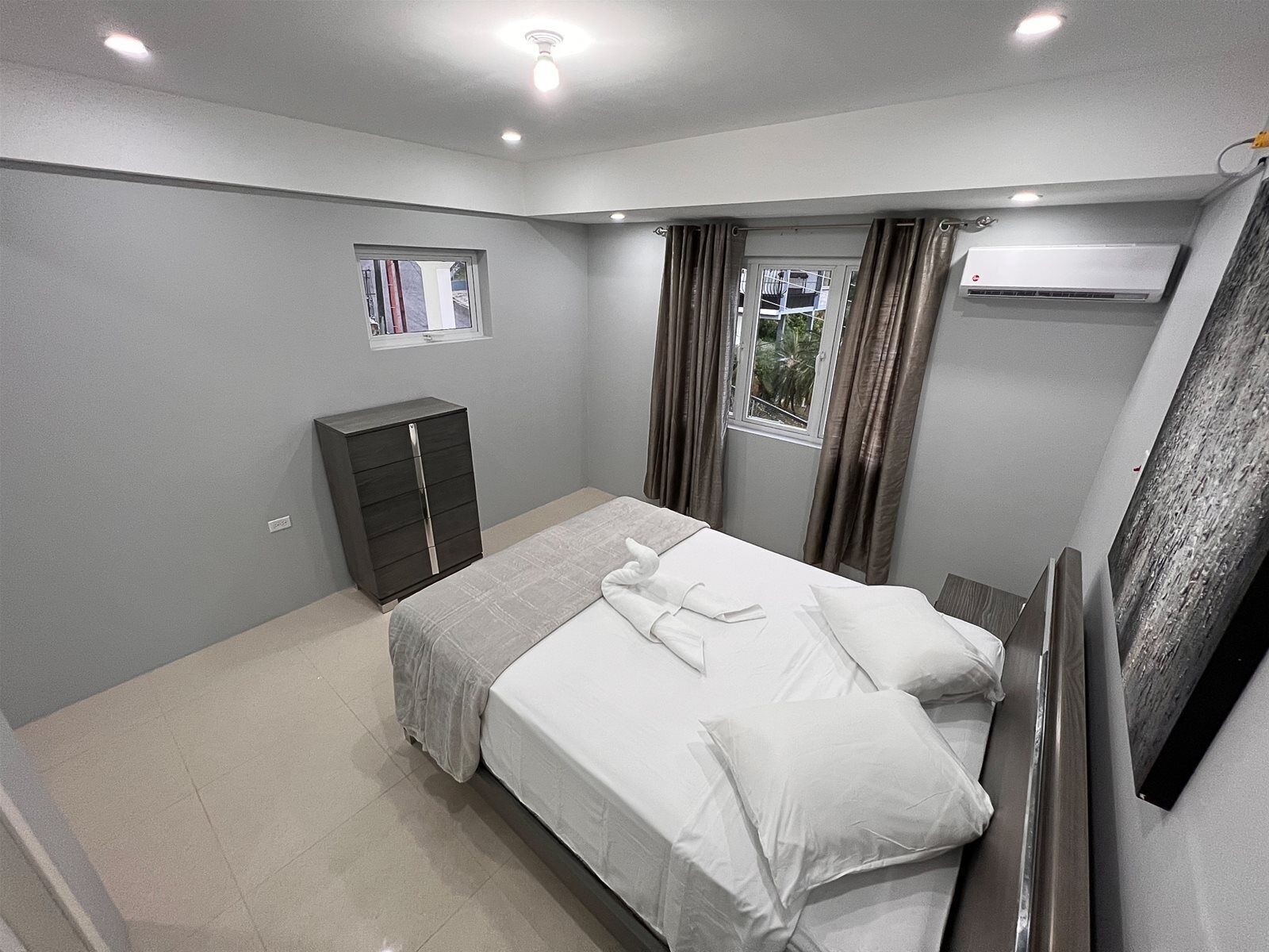 Ein Schlafzimmer mit Bett, Kleiderschrank, einem Fenster mit Vorhängen und einer Klimaanlage.