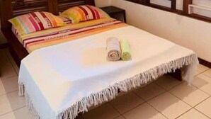 Un dormitorio con cama, ventana con contraventanas, techo de madera y una estantería con objetos.