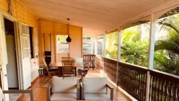 Un área de estar techada al aire libre con mesas y bancos de madera, una mesita con bandeja y vistas a follaje a través de la barandilla.