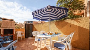 An outdoor patio with a round table, chairs, and a striped umbrella. - L'équinoxe - Charmant logement 150m de la plage (Leucate)