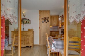 A cozy room with wooden furniture, a dining table set for two, and a kitchen area with wooden cabinets.