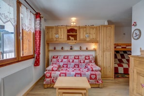 A cozy room with a wooden sofa bed, a small table, and a window with curtains.