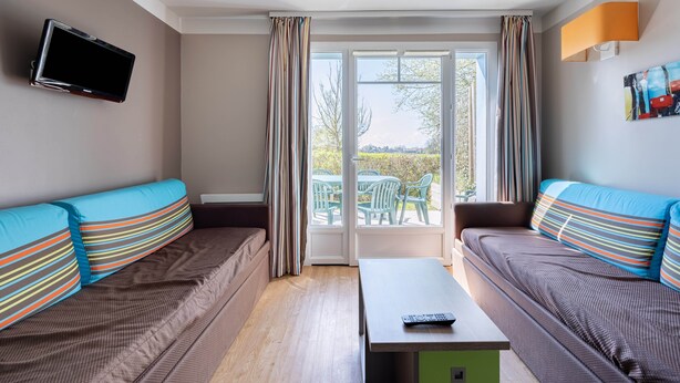 A modern room with two sofas, a flat-screen TV, a table, and a sliding glass door leading to an outdoor area with chairs. - Courlis Cendré - Two Bedroom House, Sleeps 7 (Courseulles-sur-Mer)