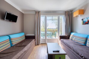 A modern room with two sofas, a flat-screen TV, a table, and a sliding glass door leading to an outdoor area with chairs. - Courlis Cendré - Two Bedroom House, Sleeps 7 (Courseulles-sur-Mer)