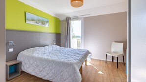 A bedroom with a bed, a chair, a painting, and a window. - Courlis Cendré - Two Bedroom House, Sleeps 7 (Courseulles-sur-Mer)