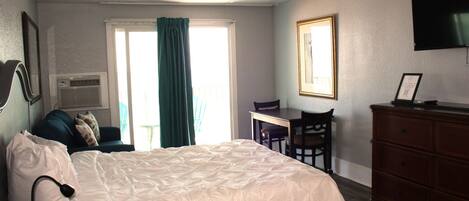 A hotel room with a bed, a desk, a chair, a dresser, a TV, and a window with curtains.