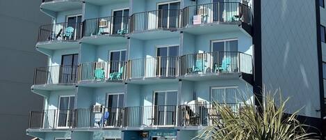 A multi-story hotel with balconies, a pool area, and a clear sky.