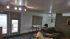 A living room with a sofa, a coffee table, a dining table, and a window with blinds. - Very quiet ground floor basement apartment in the country, big outdoor space,!!! (THAYNE, WY)