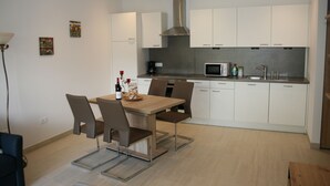 Een moderne keuken met witte kasten, een roestvrijstalen afzuigkap, een magnetron en een spoelbak. Er is een eettafel met stoelen en een kleine koffiehoek.