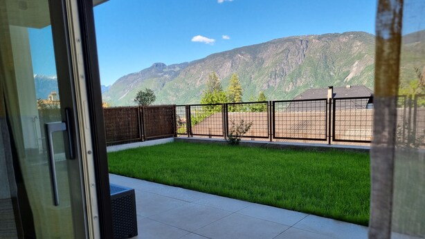 Uitzicht vanaf een balkon met een gazon, een metalen hek en een bergachtig landschap op de achtergrond.