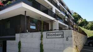Een modern gebouw met een bord waarop 'Weinberg 8' staat, bevestigd aan een betonnen muur.