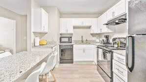 Eine moderne Küche mit weißen Schränken, einer Granit Arbeitsplatte, Edelstahlgeräten und einem gelben Toaster.