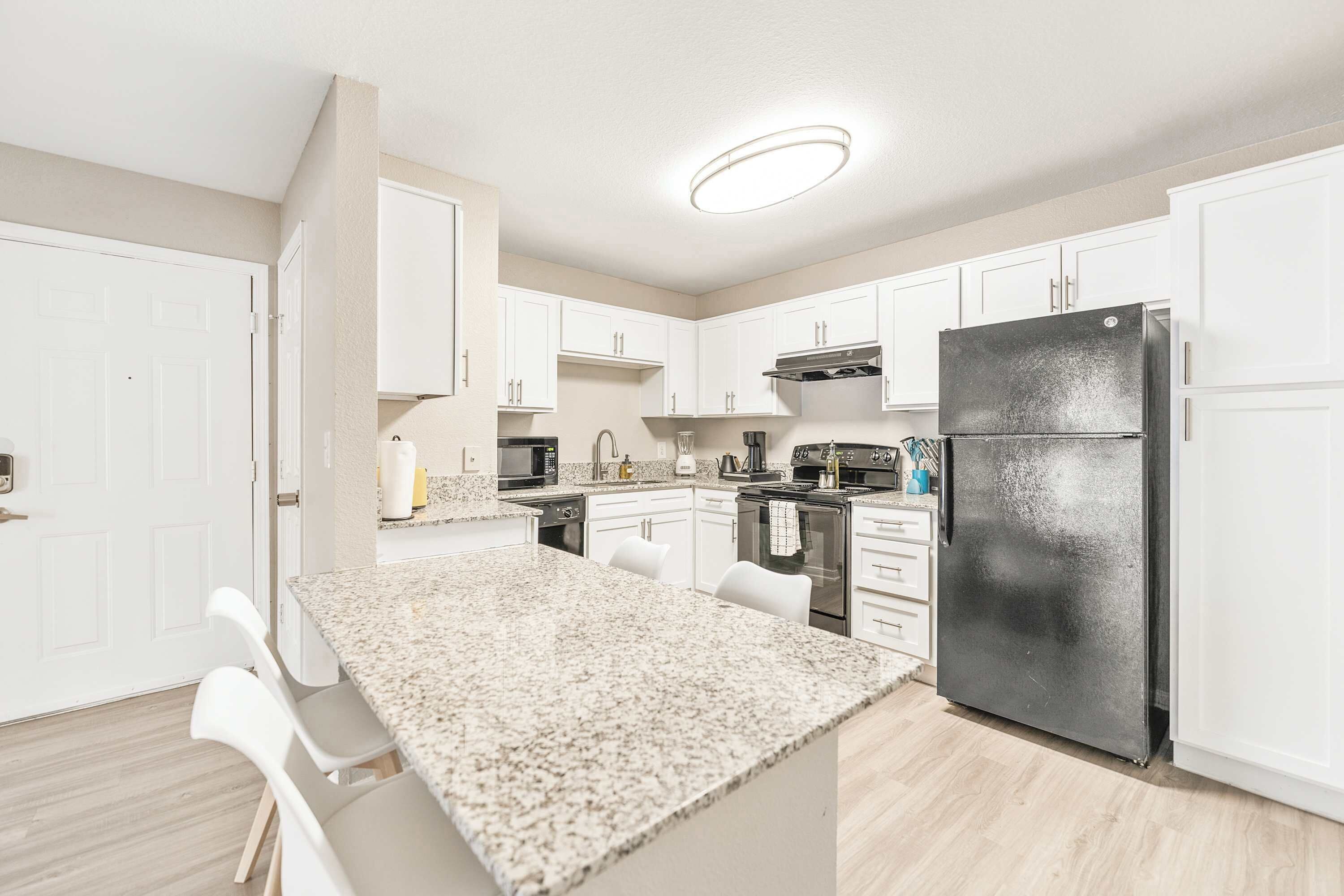 A modern kitchen with white cabinets, a granite countertop, and a black refrigerator.