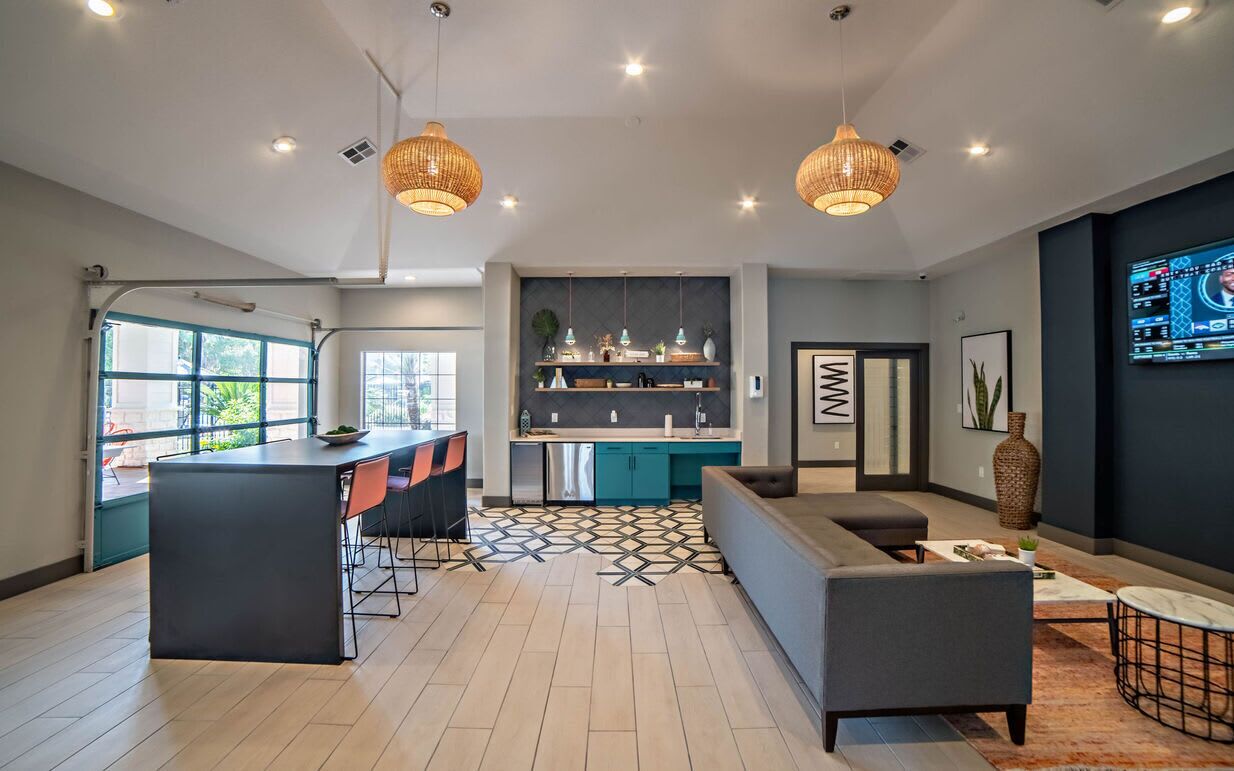 A modern kitchen with a central island, a dining area with a black table and orange chairs, and a living area with a grey sofa and a coffee table.