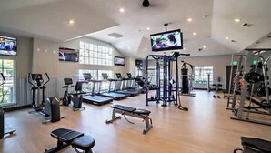 A spacious gym with treadmills, weight machines, and a television mounted on the ceiling. - Bright 2BR King Suite w Gym& close to Downtown (Austin)