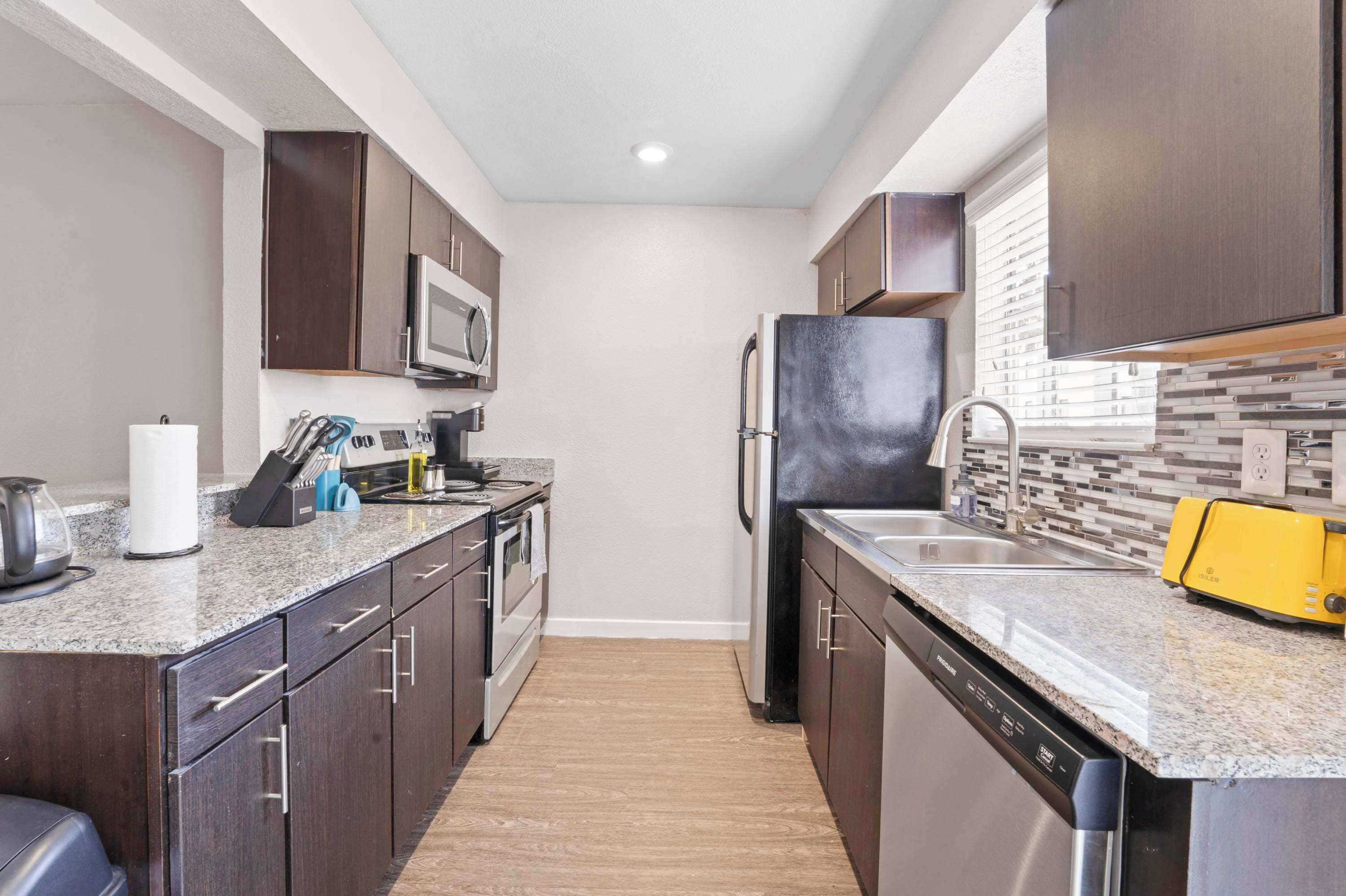 A modern kitchen with dark wood cabinets, a granite countertop, a microwave, a refrigerator, and a yellow toaster.
