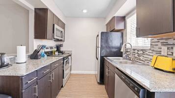 A modern kitchen with dark wood cabinets, a granite countertop, a microwave, a refrigerator, and a yellow toaster.