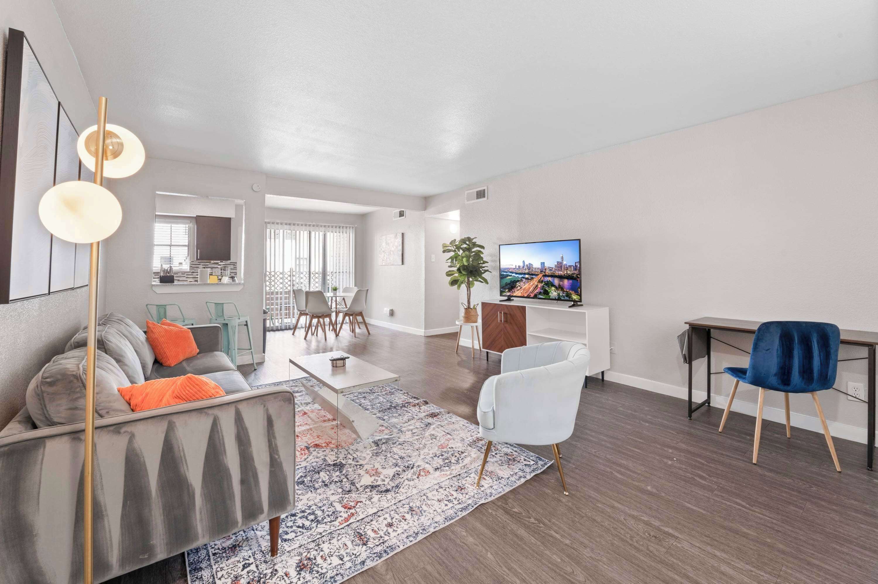 A modern living room with a sofa, coffee table, and a TV. There is a dining area with chairs and a table.