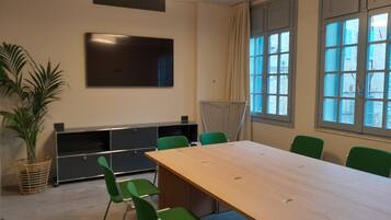 A conference room with a large table, green chairs, a flat-screen TV, and windows with a view of buildings.