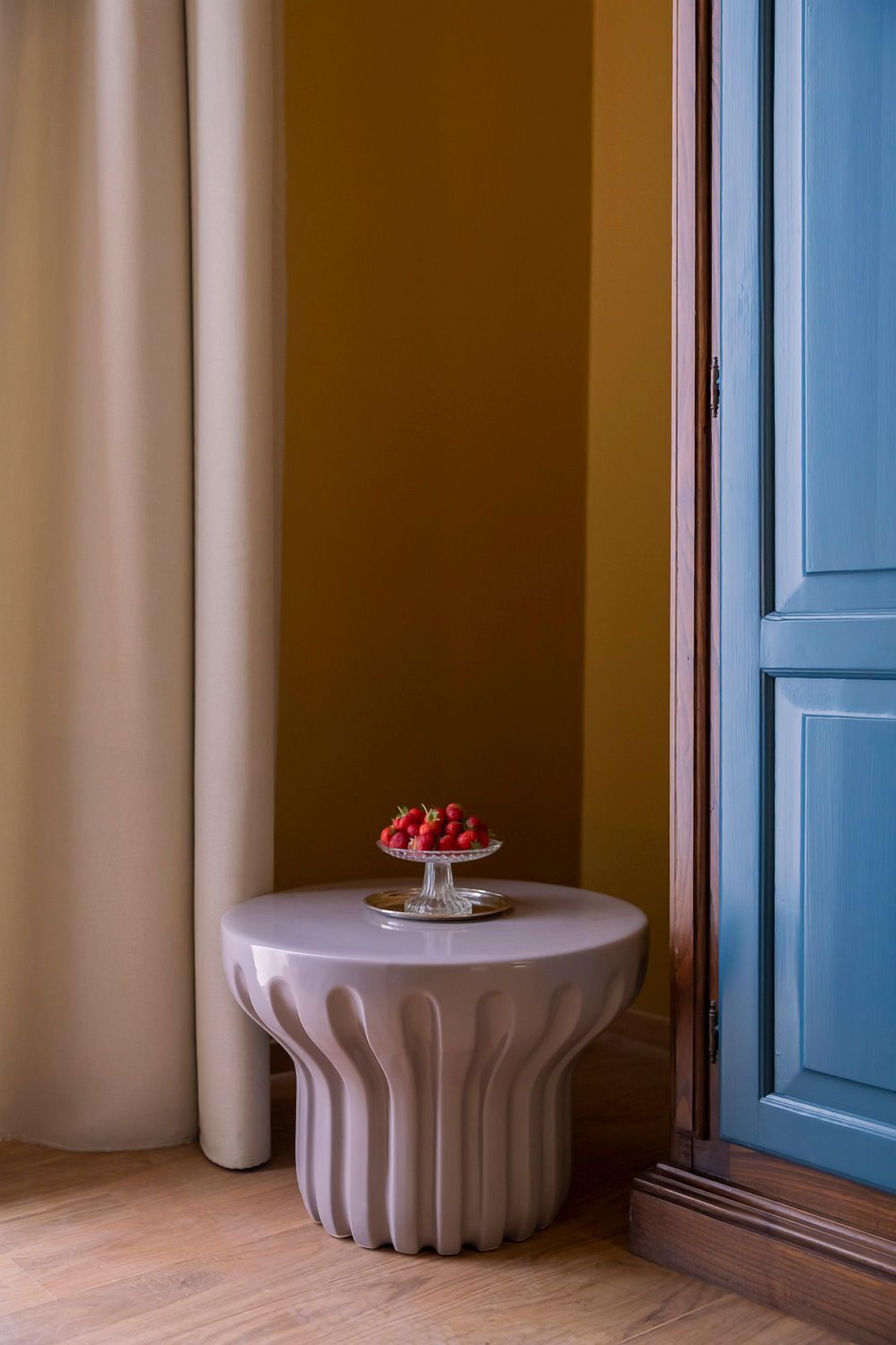Une table ronde au design original, avec un bord ondulé, placée contre un mur jaune.