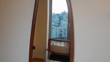 A room with a large oval mirror on the wall, a chair, and a view of a balcony with a railing.