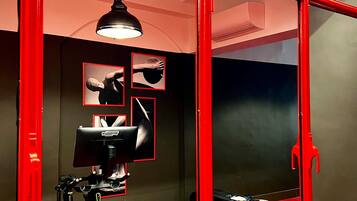 Una habitación con una ventana de marco rojo, una lámpara del techo y una bicicleta estática fijada a la pared.