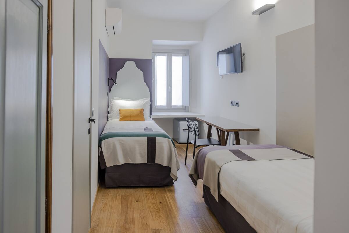 A bedroom with two beds, a desk, and a window.