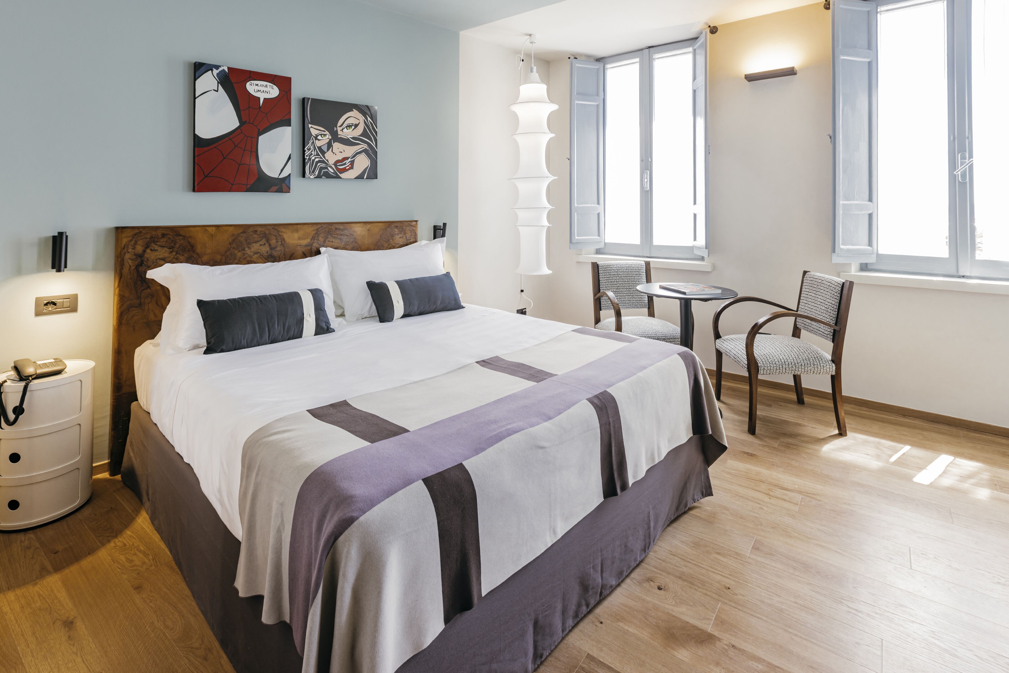 Una habitación de hotel con una cama grande, una mesita de noche con lámpara, una silla y una pequeña mesa.