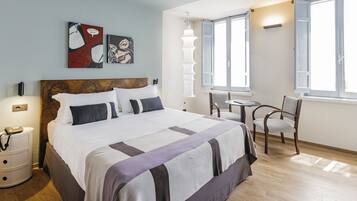 Una habitación de hotel con una cama grande, una mesita de noche con lámpara, una silla y una pequeña mesa.
