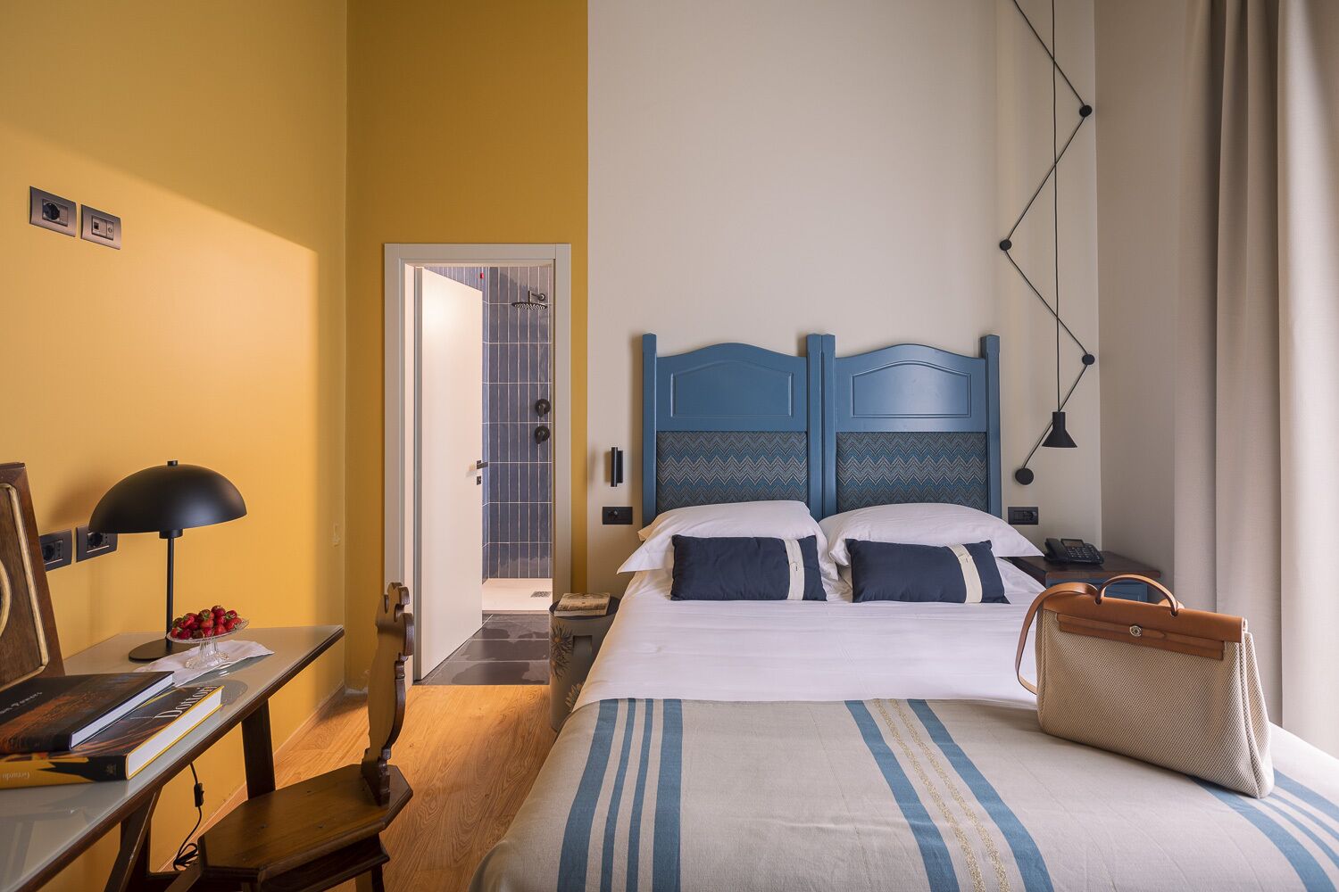A hotel room with a bed, bedside table, lamp, and a suitcase.