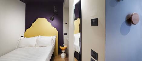 A modern hotel room with a bed, bedside table, lamp, and a mirror with a wooden door.