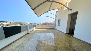 A spacious balcony with a marble floor, a covered area with a curved roof, and a view of the cityscape in the background.