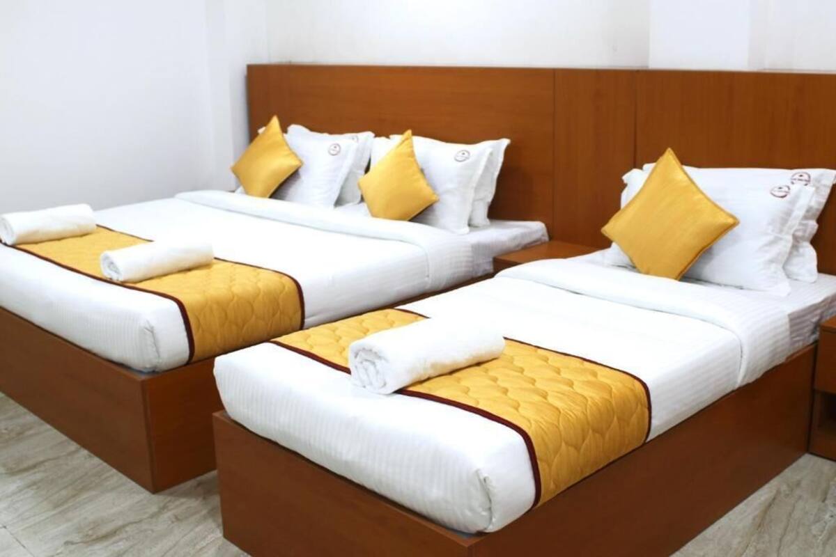 Deux lits simples avec des têtes de lit en bois, du linge de lit blanc et des touches de couleur jaune.