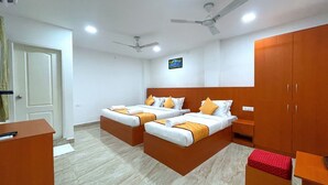 A hotel room with two beds, a desk, a wardrobe, and a ceiling fan.