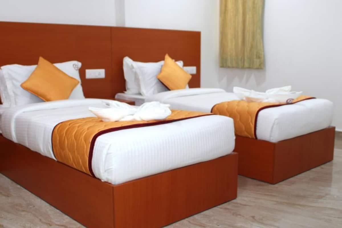 Deux lits avec des têtes de lit en bois, une literie blanche et des touches de couleur orange.