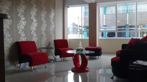 Un espacio lounge moderno con papel tapiz estampado, una mesa de centro de vidrio y sillones tapizados en rojo y negro.