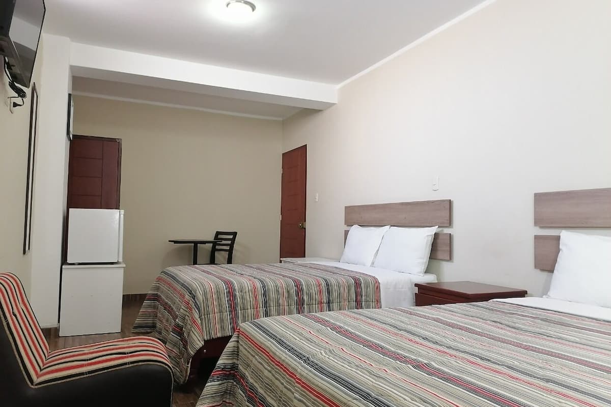 Een hotelkamer met twee bedden, een kleine tafel, een stoel, een koelkast en een televisie.