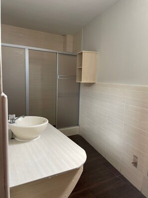A bathroom with a white sink, a shower, and a wooden cabinet. - Hotel Plaza Barranca (Barranca)
