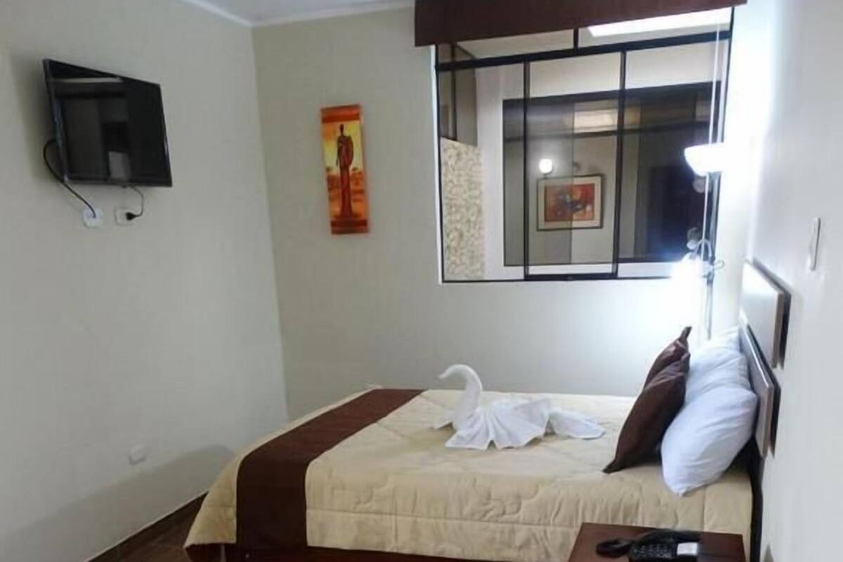 Een hotelkamer met een bed, een klein nachtkastje met een telefoon, een gestreepte stoel, een aan de muur bevestigde televisie en een raam met uitzicht.