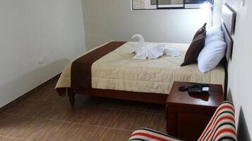 Habitación de hotel con cama, una mesita de noche con teléfono, una silla a rayas, televisor montado en la pared y ventana con vistas.