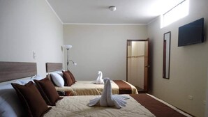 Habitación de hotel con dos camas, cada una con almohadas marrones y blancas, y una toalla con forma de cisne en la cama al frente.