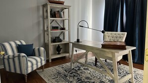 Een werkruimte met een gestreept fauteuil, een boekenplank, een bureau met een schaakbord en een scheepsmodel.