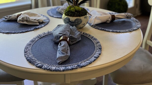Een ronde eettafel met een centrale vaas witte orchideeën, omringd door placemats en opgevouwen servetten.