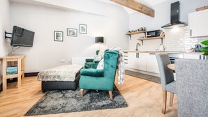 Uma sala de estar moderna com uma poltrona verde-azulado, uma mesinha e uma televisão de tela plana sobre um suporte de madeira.
