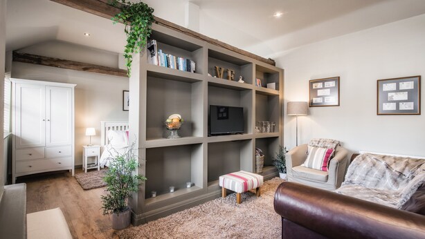 A living room with a large bookshelf, a sofa, a small table, and a lamp. - The Old Tractor Shed (Driffield)
