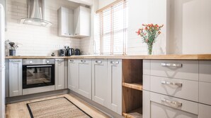 A modern kitchen with white cabinetry, a built-in oven, and a wooden countertop. - The Old Tractor Shed (Driffield)